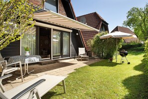 Un patio con mobiliario exterior, una parrilla y una zona cubierta con mesa y sillas.