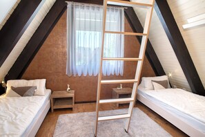 Dormitorio tipo loft con dos camas, una escalera de madera, un ventanal con cortinas y una mesita de noche con lámpara.