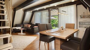Un interior moderno con zona de comedor, un conjunto de sofás y una cocina visible a través de una ventana.