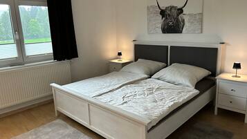 Une chambre à coucher comprenant un lit, deux tables de chevet, une fenêtre avec des rideaux, un radiateur et une œuvre d’art représentant un taureau accrochée au mur.