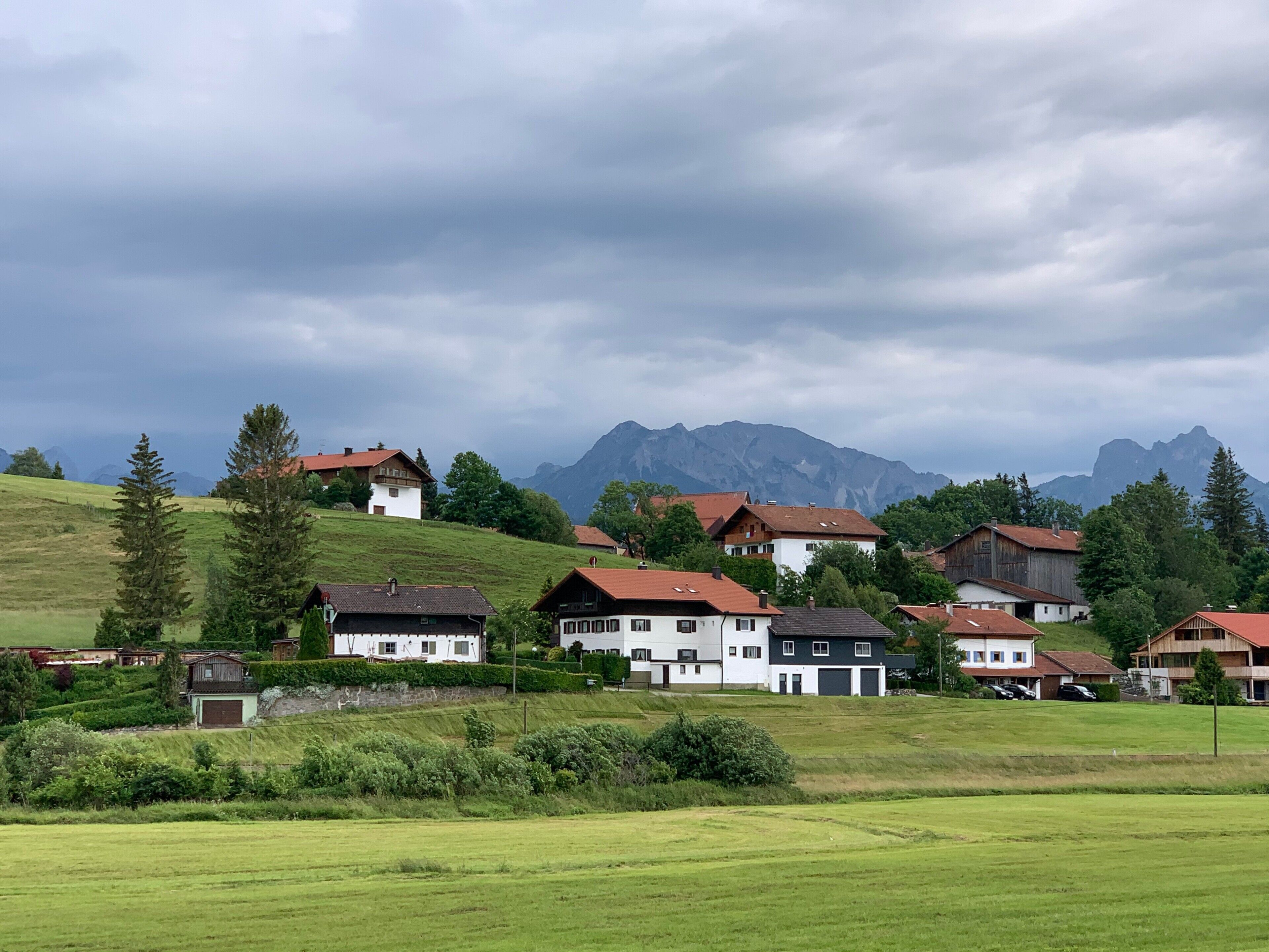 A rural village with houses on a hillside, surrounded by greenery and mountains in the background.
