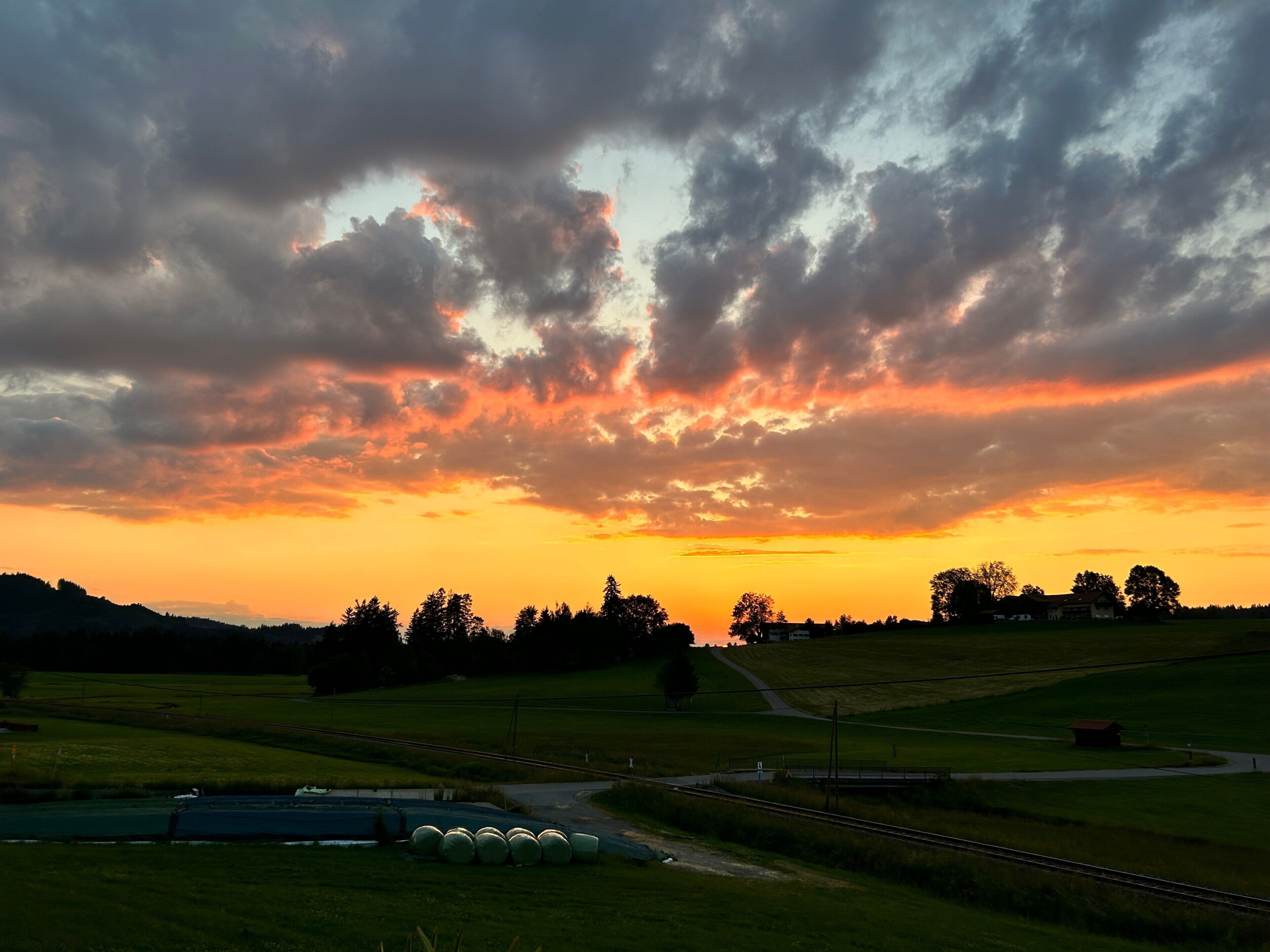 Un paysage rural avec un coucher de soleil, des champs et une voie ferrée.