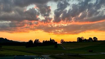 A rural landscape with a sunset, fields, and a railway track.