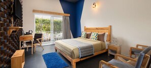 A bedroom with a bed, a desk, a chair, a TV, and a balcony with a view of greenery. - Justa Lazy Haven Corbett, Uttarakhand (Ramnagar)