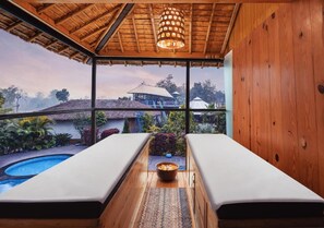 A spa room with two massage tables, a small pool, and a view of a traditional building and landscape. - Justa Lazy Haven Corbett, Uttarakhand (Ramnagar)