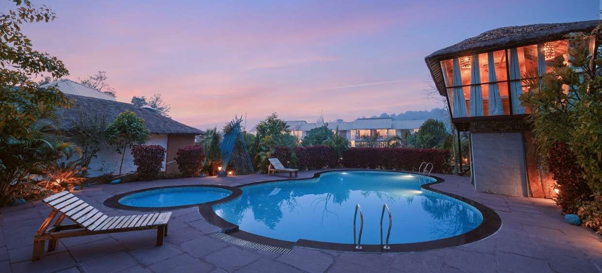 A pool area with two pools, lounge chairs, and a building with a thatched roof.