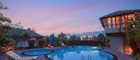 Un área de piscina con sillones de descanso y un edificio de diseño singular.