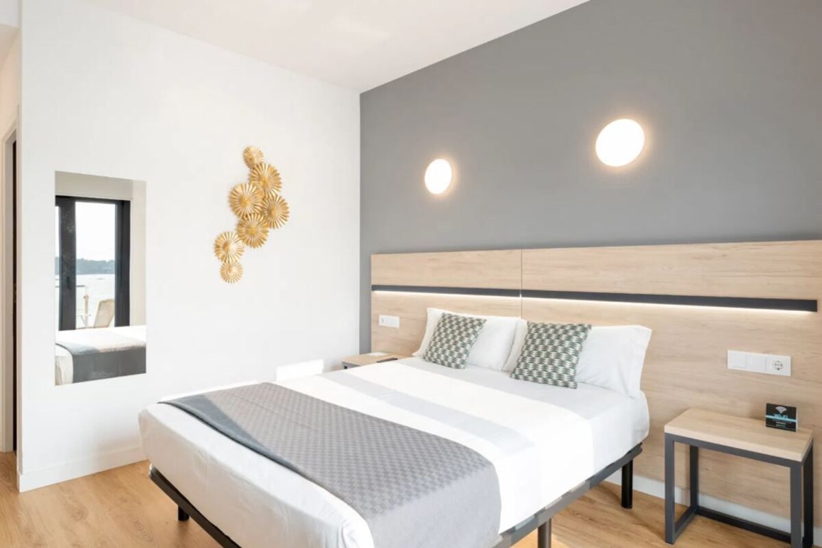 Una habitación de hotel moderna con una cama grande, mesitas de noche, un espejo y detalles decorativos en la pared.