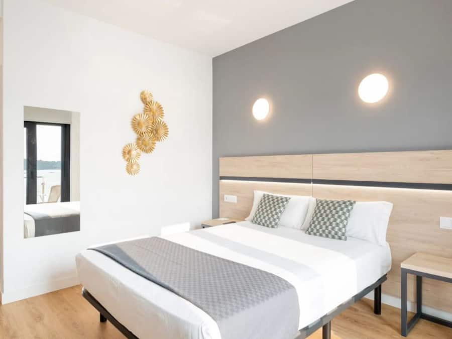 Un dormitorio moderno con una cama grande, mesitas de noche, un espejo y un elemento decorativo en la pared.