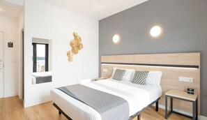Una habitación de hotel moderna con una cama grande, mesitas de noche, un espejo y detalles decorativos en la pared.