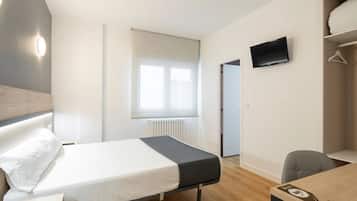 Habitación de hotel con cama, escritorio, silla, televisor y ventana con persianas.