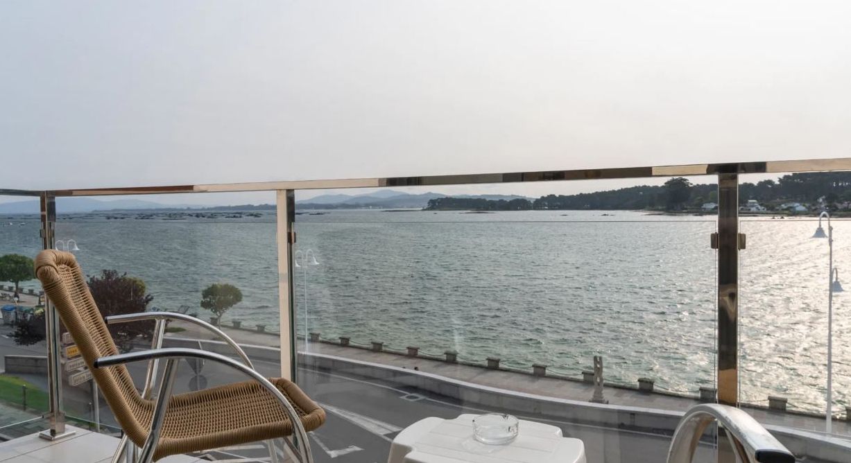 Een balkon met uitzicht op een wateroppervlak, rieten stoelen, een tafel en een leuning.