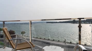 Een balkon met uitzicht op een wateroppervlak, rieten stoelen, een tafel en een leuning.