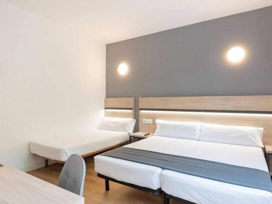 A hotel room with a bed, a desk, and a chair. There are two bedside tables with lamps.