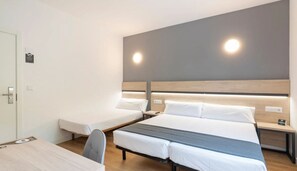 Une chambre d’hôtel avec un lit, un bureau et une chaise. Il y a deux tables de chevet avec des lampes.