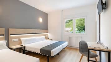 A modern hotel room with a large bed, bedside tables, a desk with a chair, and a window with a view of greenery.