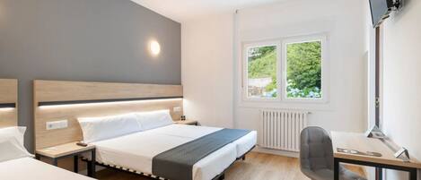 A modern hotel room with a large bed, bedside tables, a desk with a chair, and a window with a view of greenery.
