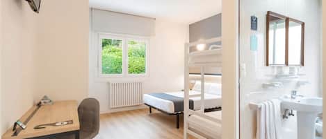 Una stanza con un letto a castello, una scrivania con sedia, una finestra vista verde e un bagno con lavandino e specchio.