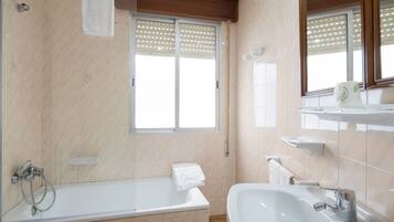 Un baño moderno con bañera, lavamanos y ventana con persianas.