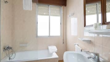 Un baño moderno con bañera, lavamanos y ventana con persianas.