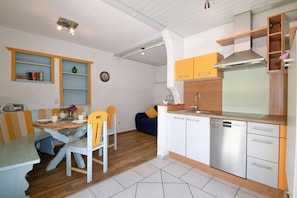Una cocina compacta con lavavajillas, un comedor con mesa y sillas, y una estantería empotrada.