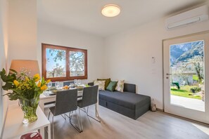 Un salon moderne comprenant un canapĂ©, une table Ă manger, des chaises et une grande fenĂȘtre donnant sur un jardin.