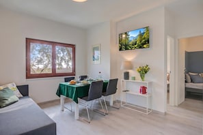 A dining area with a table set for two, a TV mounted on the wall, and a window with a view of trees. - Relais Nanzello Garda (Limone sul Garda)