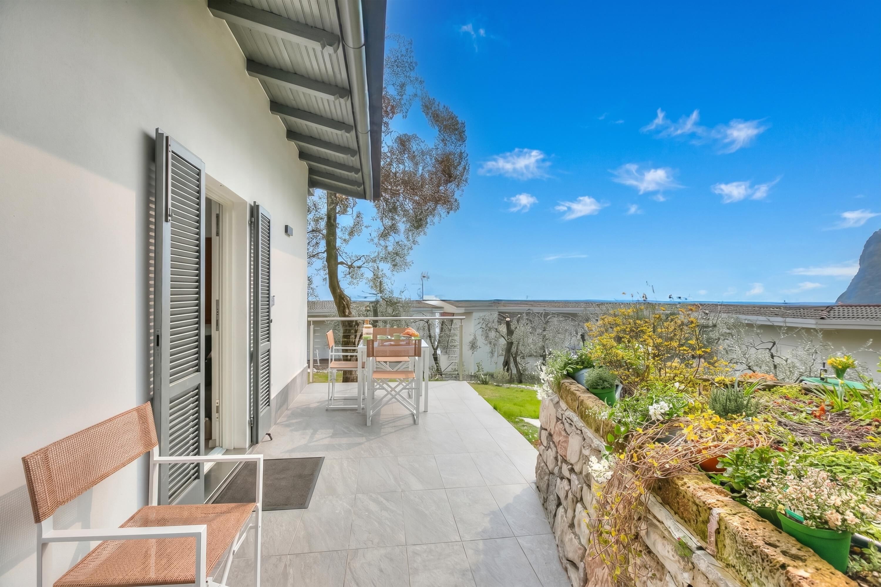 A patio with outdoor furniture, a stone wall with plants, and a view of the sea.