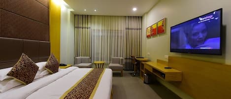 A hotel room with a large bed, a TV, a desk, and a seating area.