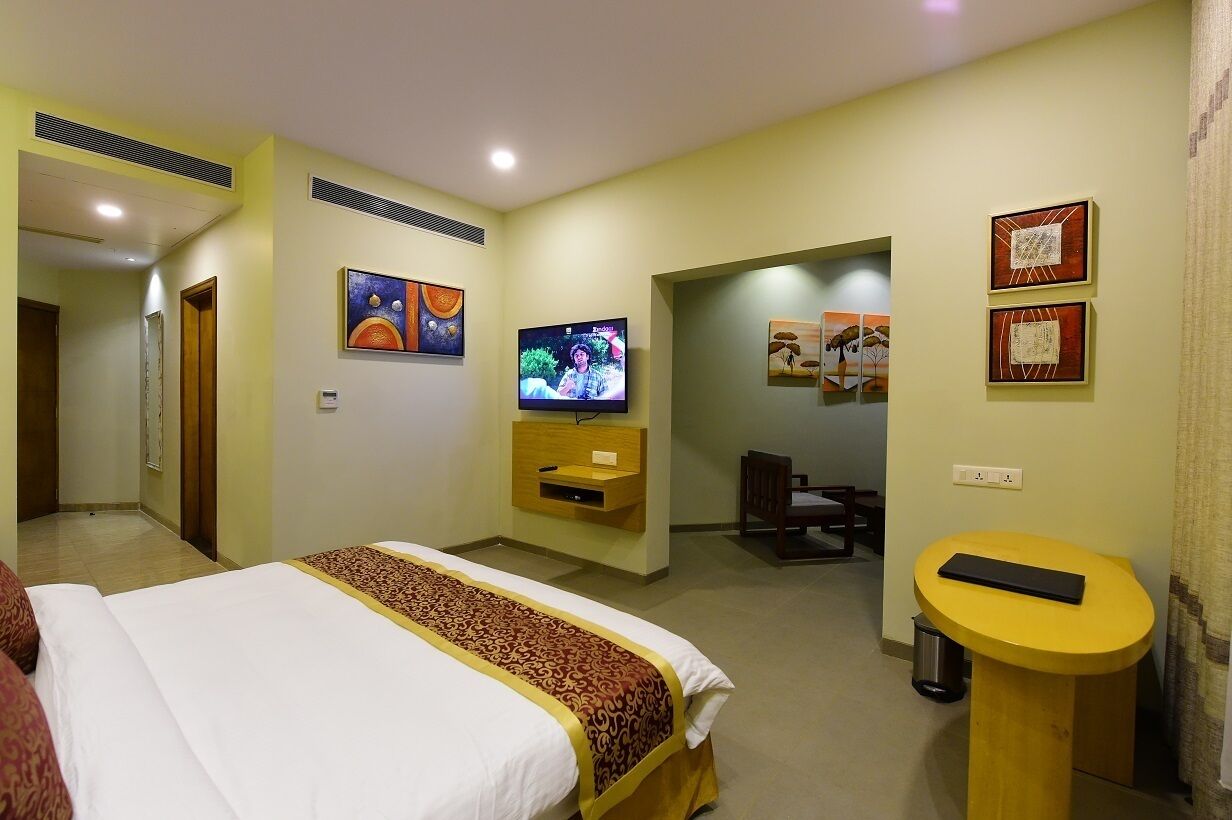 A hotel room with a bed, TV, desk, and artwork on the walls.