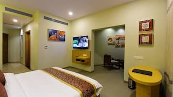 A hotel room with a bed, TV, desk, and artwork on the walls.