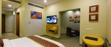 A hotel room with a bed, TV, desk, and artwork on the walls.