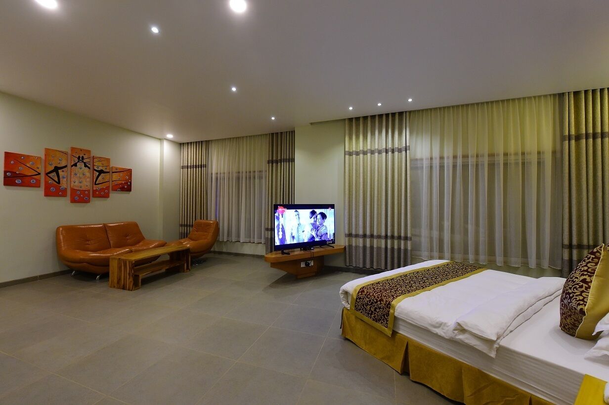 A hotel room with a bed, a sofa, a TV, and artwork on the wall.