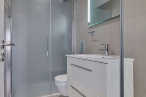 Bathroom features a glass-enclosed shower, sink, and toilet in a minimalist design.