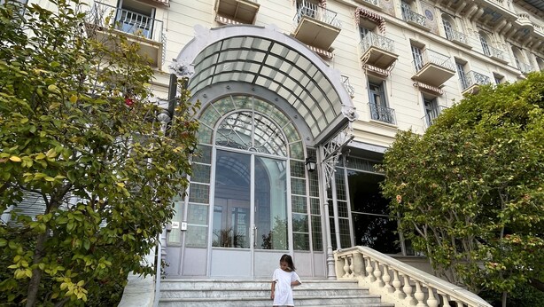 A grand building with a large arched entrance, a marble staircase, and a balcony with ornate railings.