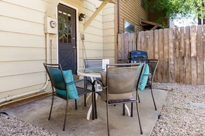 Eine Außenpatio mit einem runden Tisch, vier Stühlen, einem Grill und einem Holzzaun.