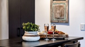 A kitchen counter with a potted plant, two glasses of champagne, and a wooden board with fruits and pastries. - `Family Beach Getaway` by Inn Paradise (Surfers Paradise)