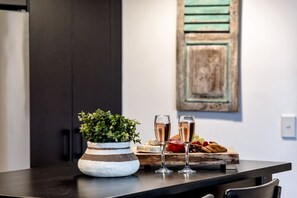 A kitchen counter with a potted plant, two glasses of champagne, and a wooden board with fruits and pastries. - `Family Beach Getaway` by Inn Paradise (Surfers Paradise)