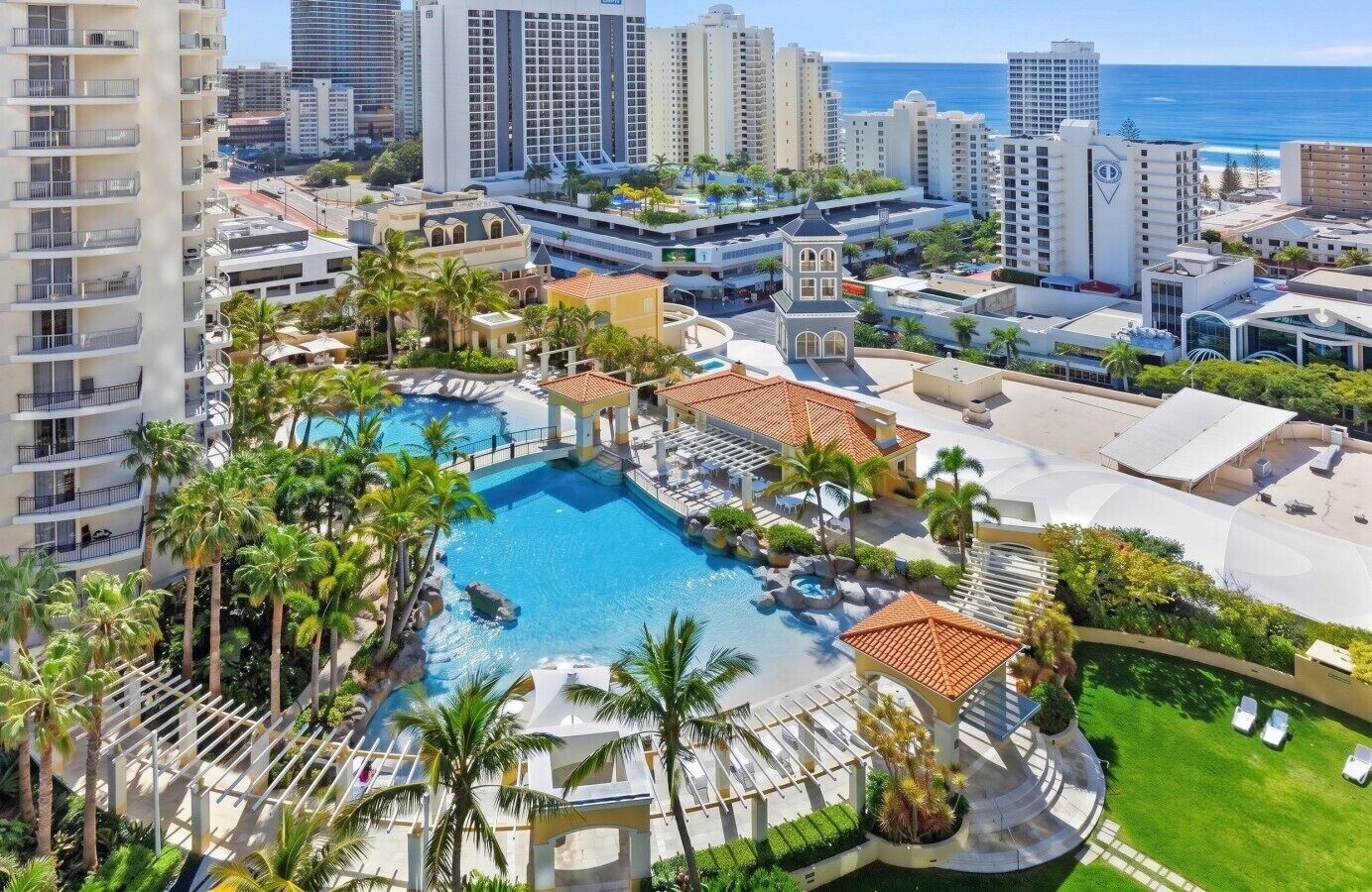 A resort with a central swimming pool, multiple buildings, and palm trees.
