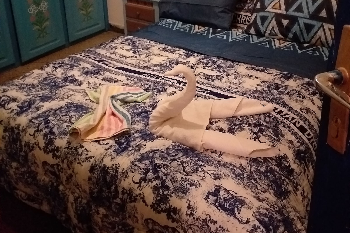Un lit avec une couvre-lit à motifs floraux, une tête de lit en bois et deux oreillers aux motifs géométriques.