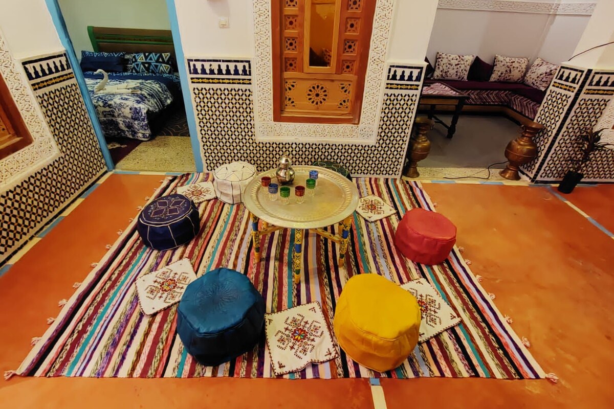 Une pièce avec un sol à motifs, une table centrale sur laquelle se trouve un plateau, et deux tabourets.