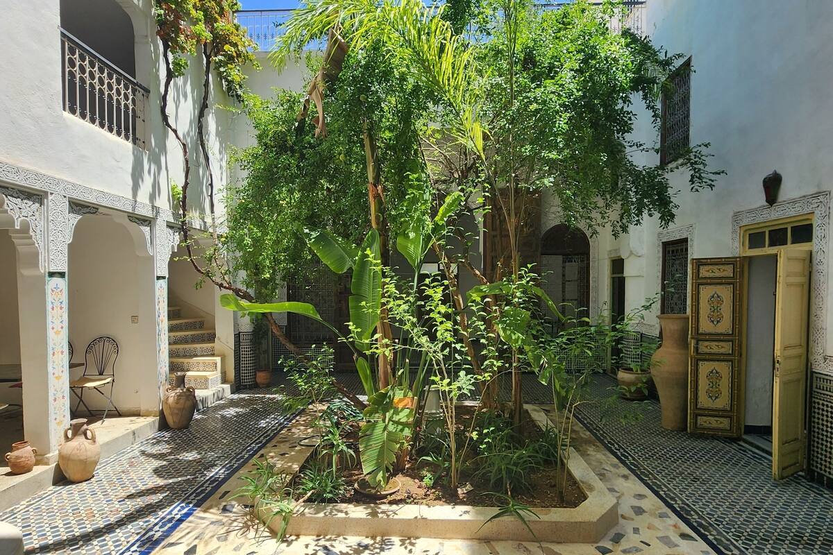 A courtyard with tiled flooring, potted plants, and architectural details like arches and doors.