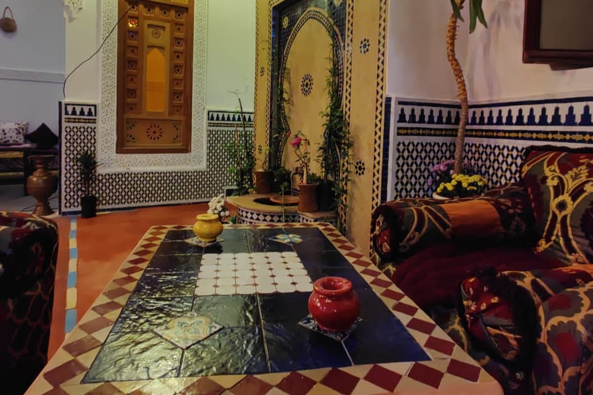 Een traditioneel Marokkaans interieur met een betegelde vloer, een centrale tafel met een rode vaas en een bank met gestreepte kussens.