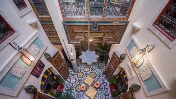 A courtyard with intricate tile work, a central fountain, and a ceiling with detailed patterns. - Fez Experience (Fes)