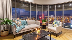 A modern living room with a large window, a sofa, a chair, a coffee table, and a potted plant. - One Thibault Residence By Itc Hospitality (Cape Town)