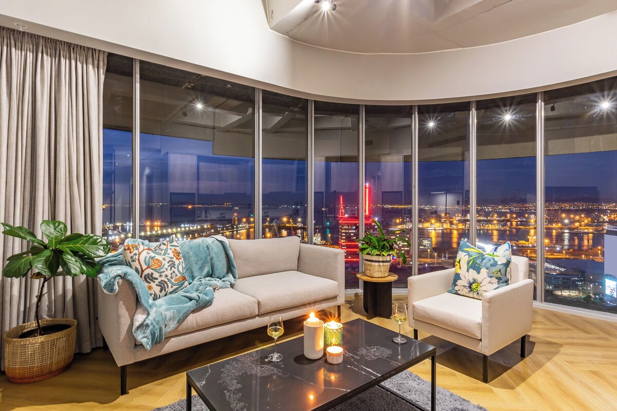 A modern living room with a large window, a sofa, a chair, a coffee table, and a potted plant.
