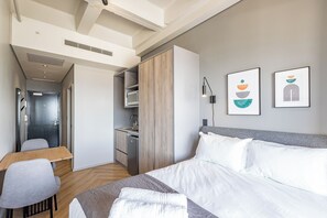 A hotel room with a bed, a desk, a chair, a wardrobe, a microwave, and artwork on the wall. - One Thibault Residence By Itc Hospitality (Cape Town)