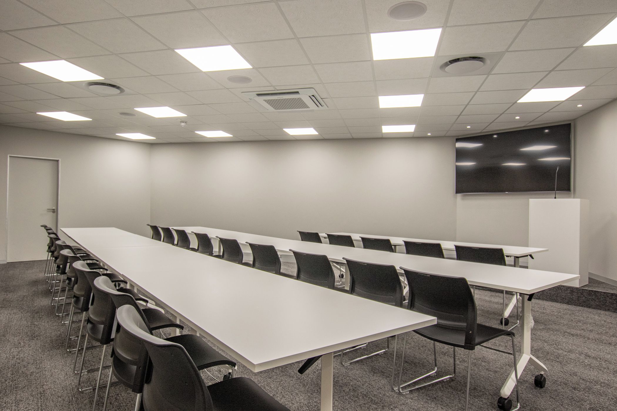 A conference room with a long table, chairs, a whiteboard, and a projector screen.