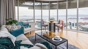 A modern living room with a large window, a sofa, a coffee table, and a dining area.