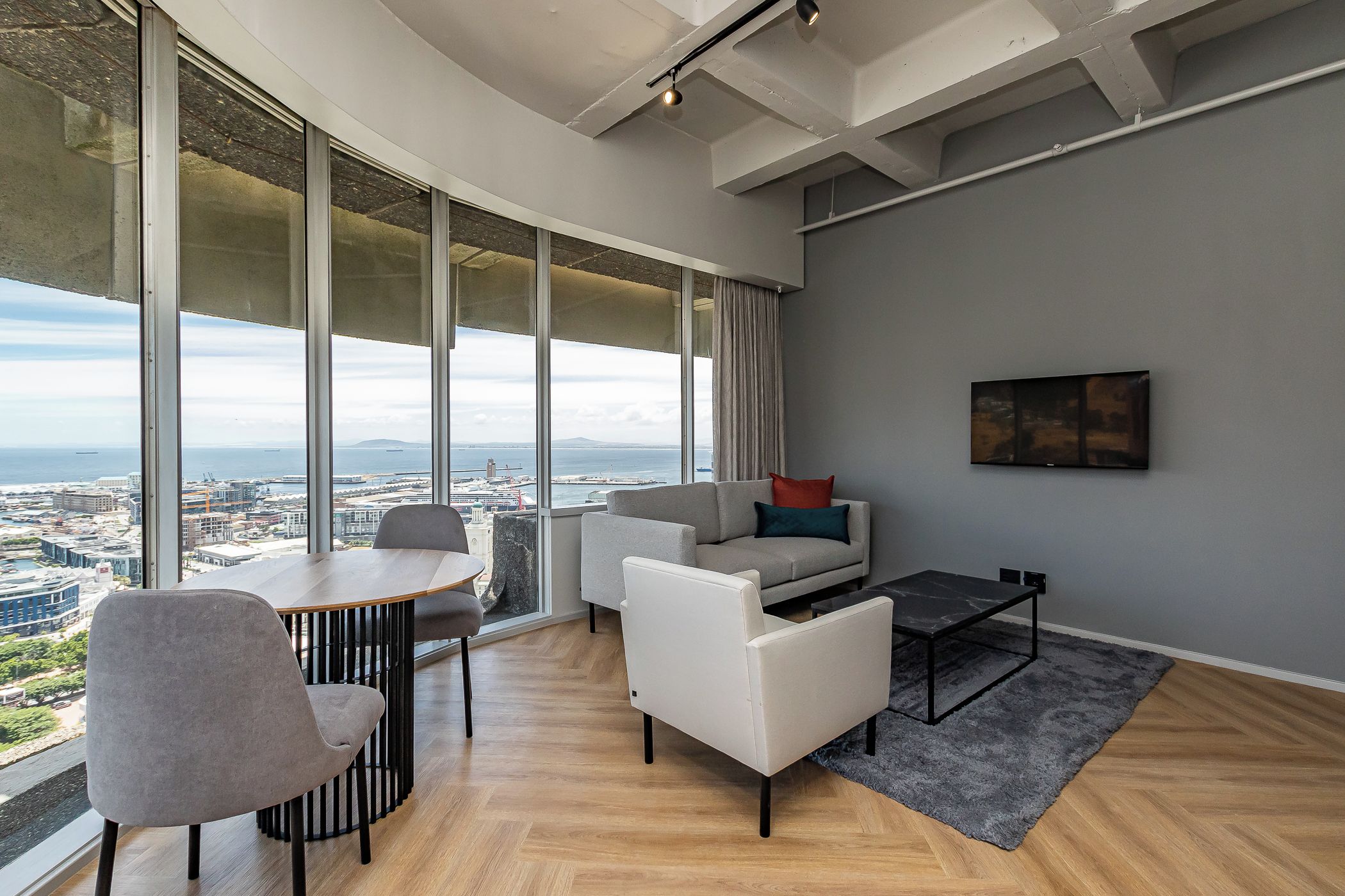 A modern living room with a large window, a sofa, a coffee table, and a dining table.